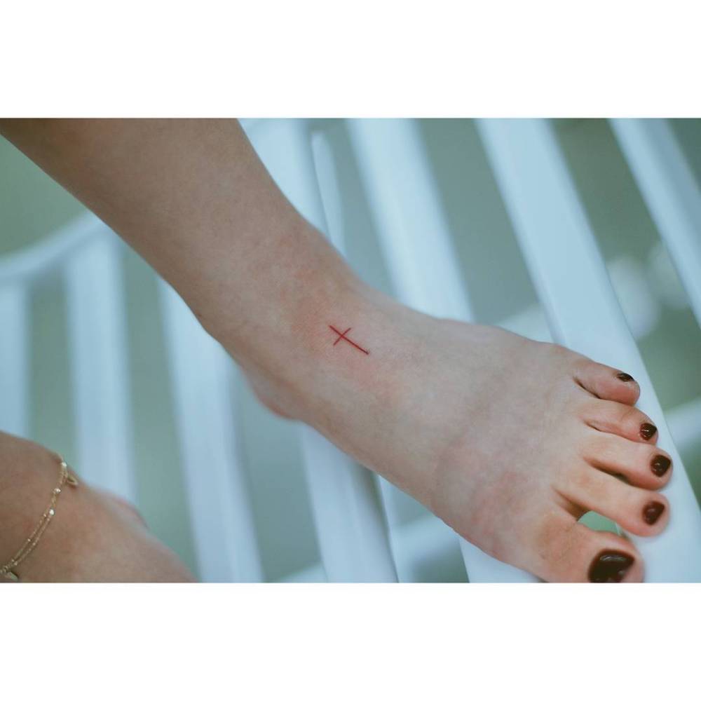Minimalistic red cross tattoo located on the foot.