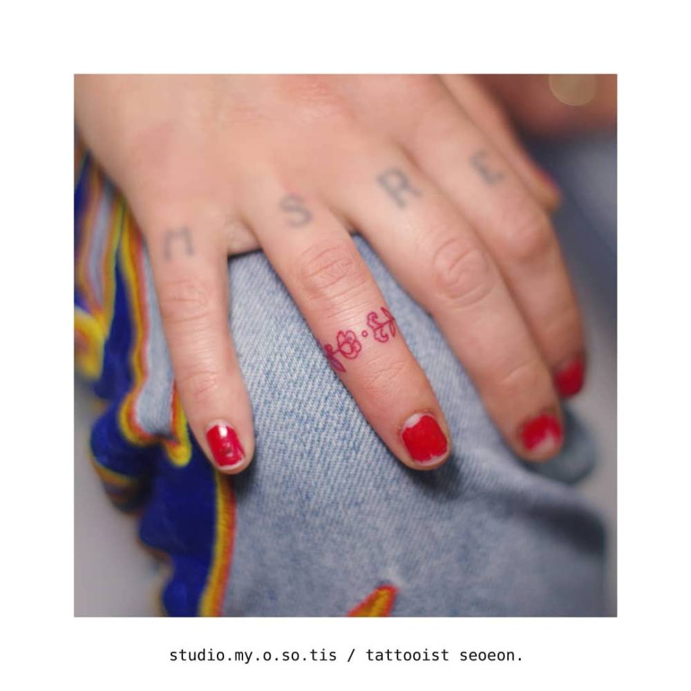Tiny minimalistic red flowers tattoo located on the finger.