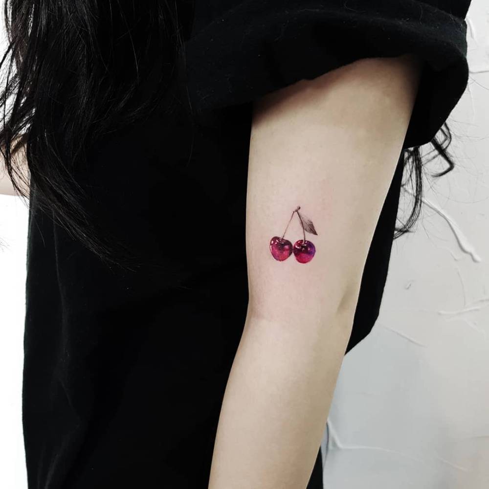 Micro-realistic style cherries tattooed on the upper arm.