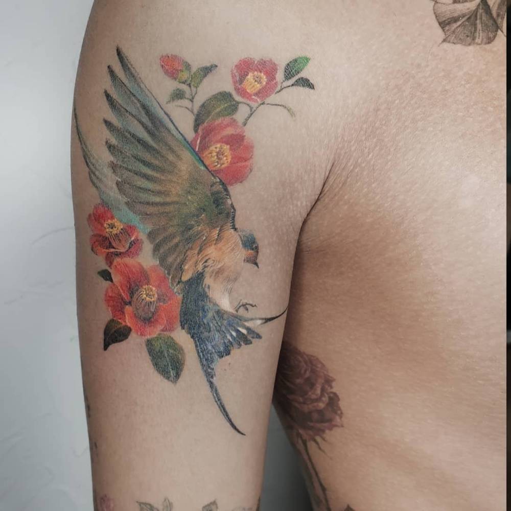 Watercolor style swallow and camellias tattoo located on the upper arm.