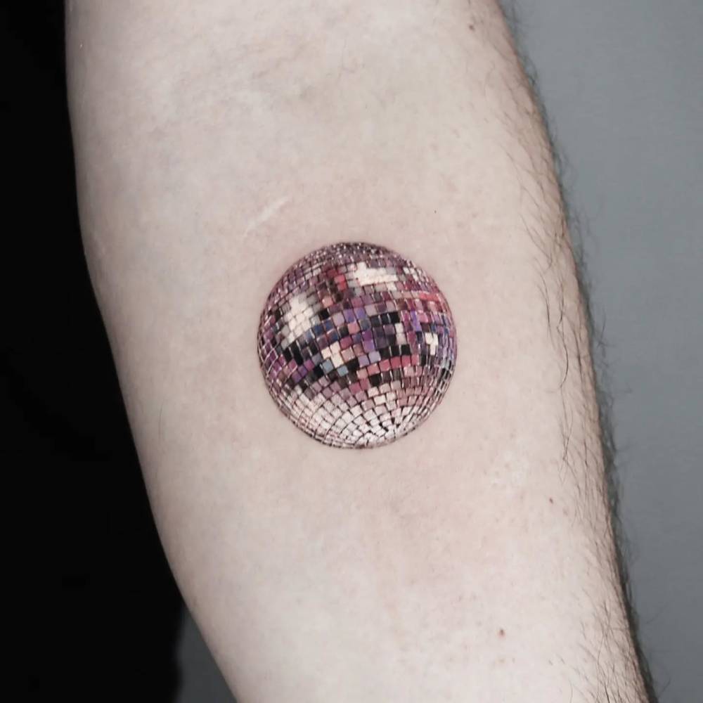 Disco ball tattoo placed on the inner forearm, micro-realistic style.
