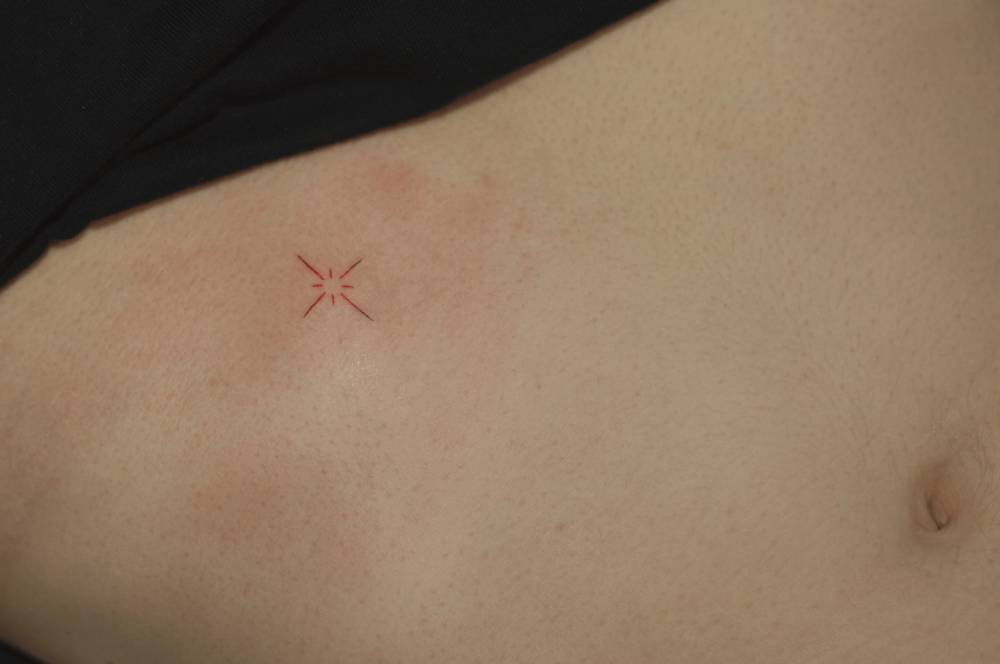 Minimalistic style north star in red ink tattooed on the rib.
