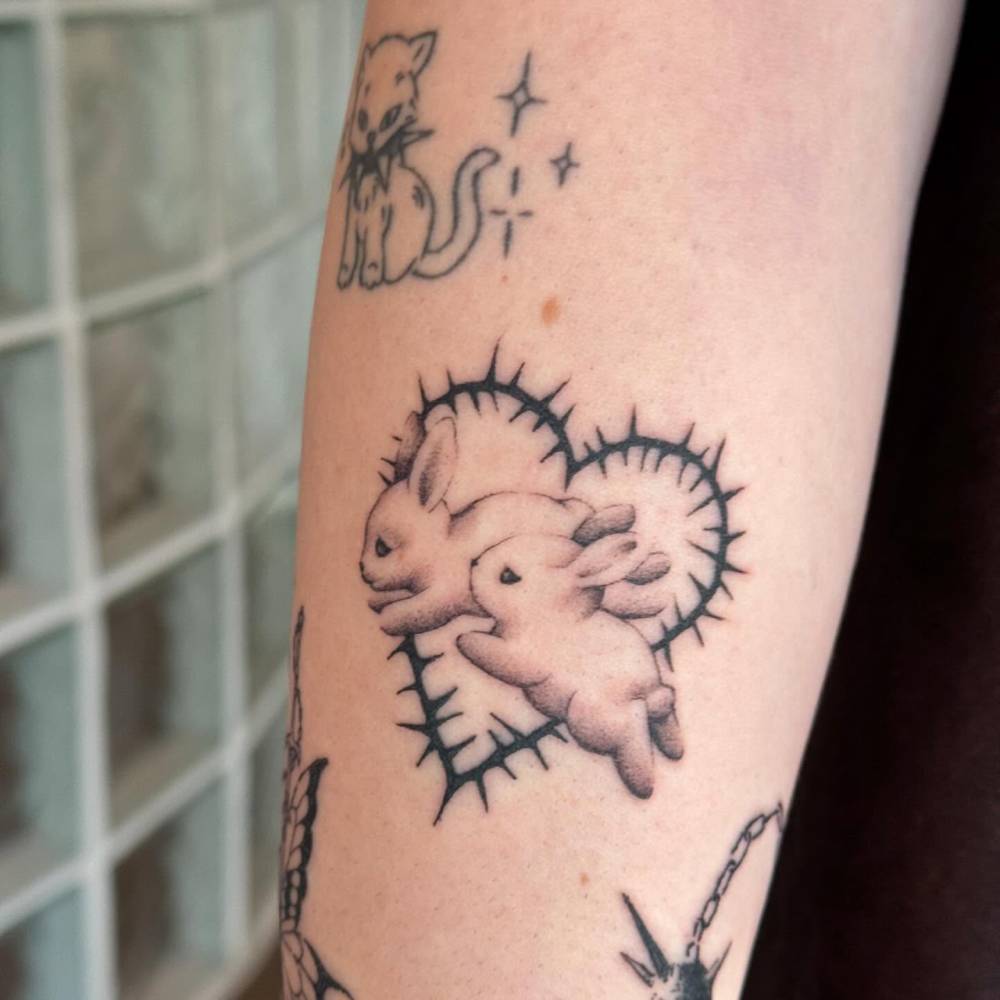 Heart of thorns and little bunnies tattooed on the forearm.