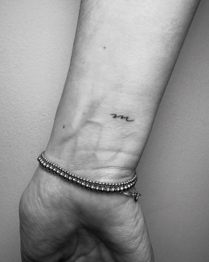 Minimalistic style letter "M" tattoo located on the wrist.