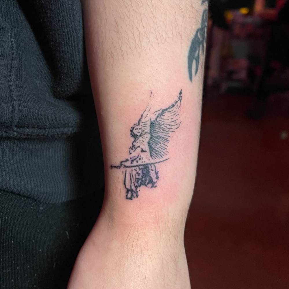 Stencil style guardian angel tattoo located on the wrist.