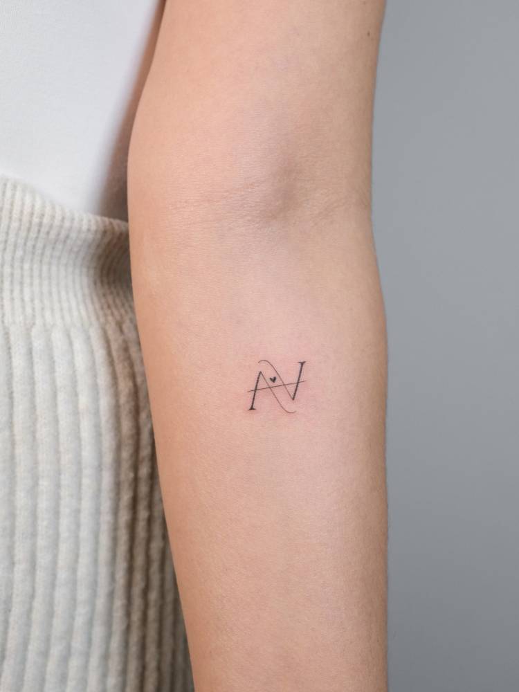 Letter "A" tattoo in serif font located on the inner forearm.