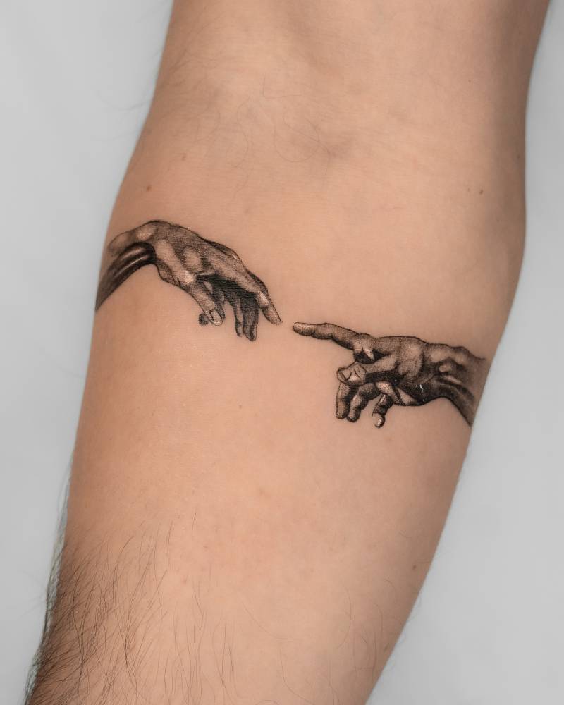 'Creation of Adam' hands tattooed on the inner forearm.