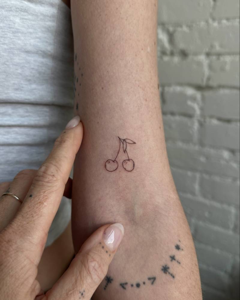 Fine line style cherries tattoo placed on the bicep.