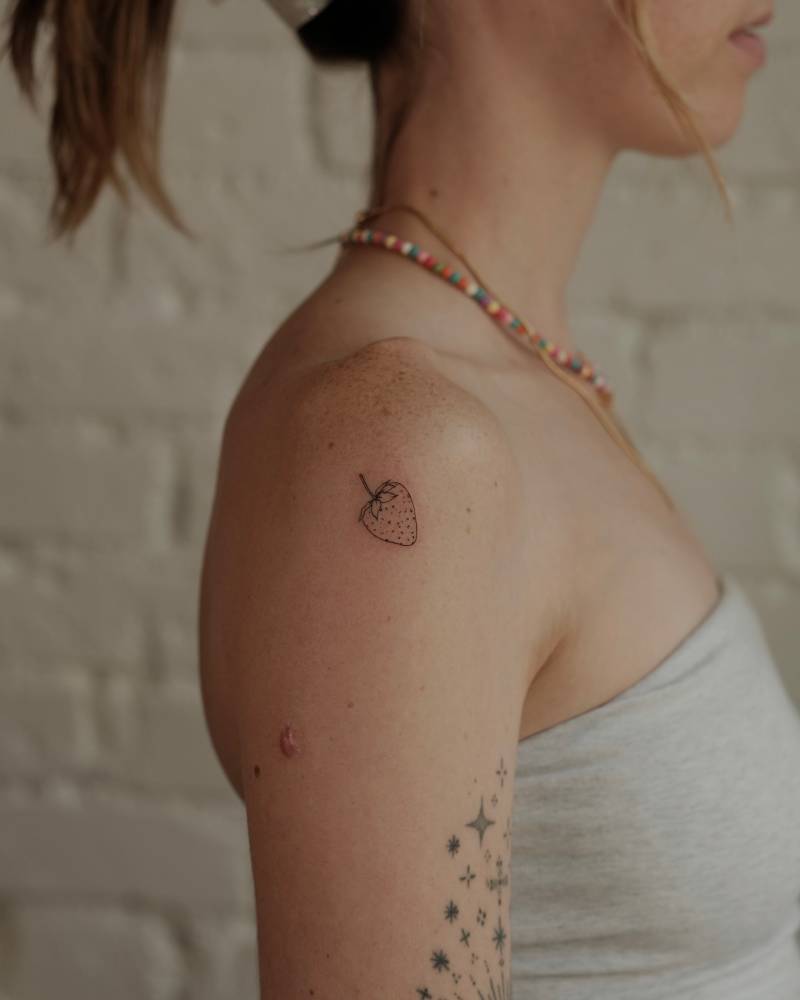 Strawberry tattoo in fine line style located on the shoulder.