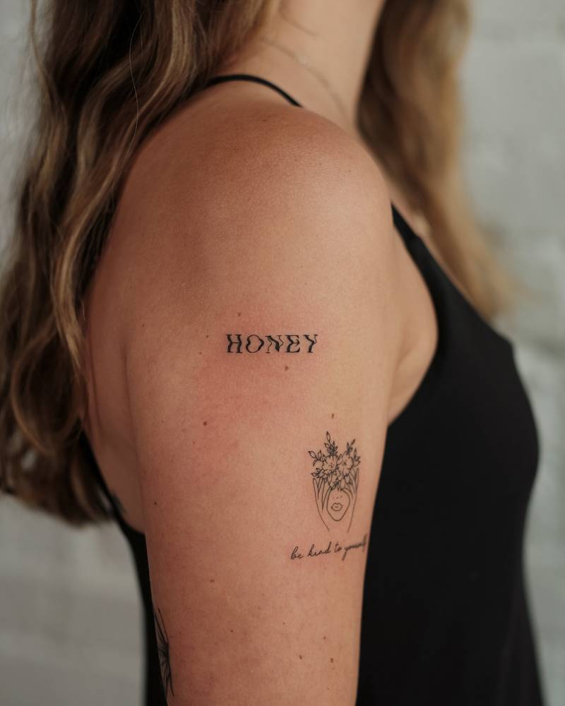 Lettering tattoo of the word "honey" located on the upper arm.