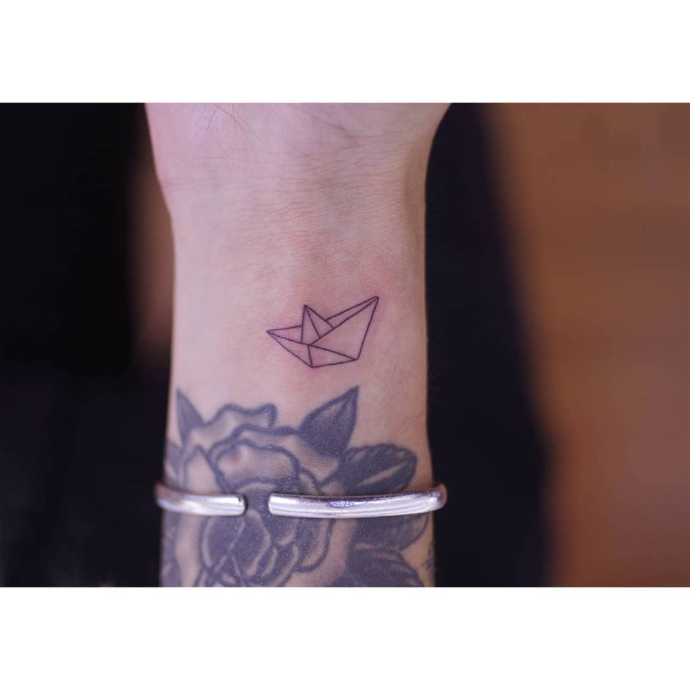 Origami boat tattoo located on the wrist, fine line style.
