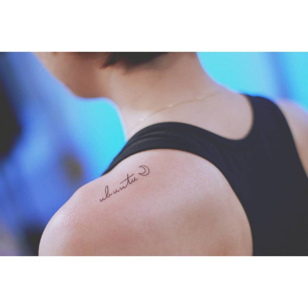 Word "ubuntu" and minimalistic crescent moon tattooed on the top of shoulder.