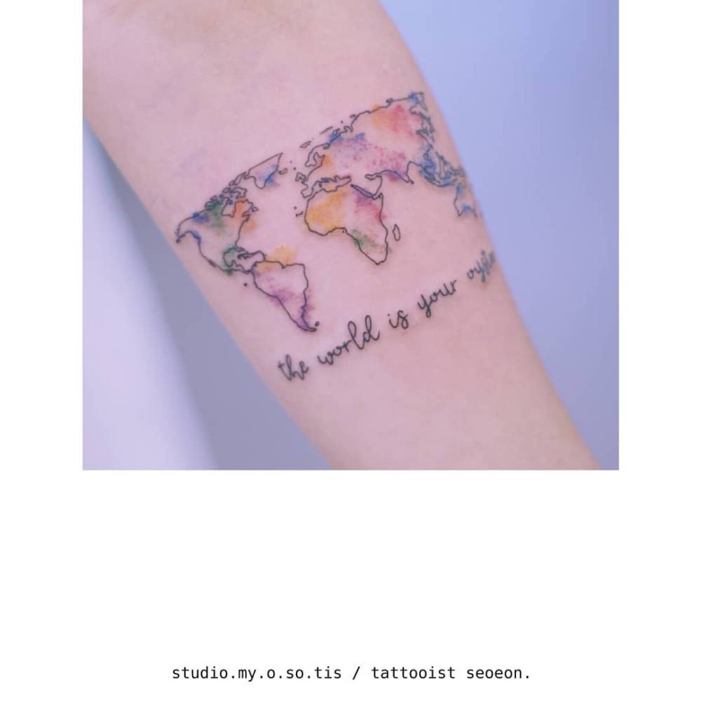 Watercolor style world map tattoo located on the inner forearm.