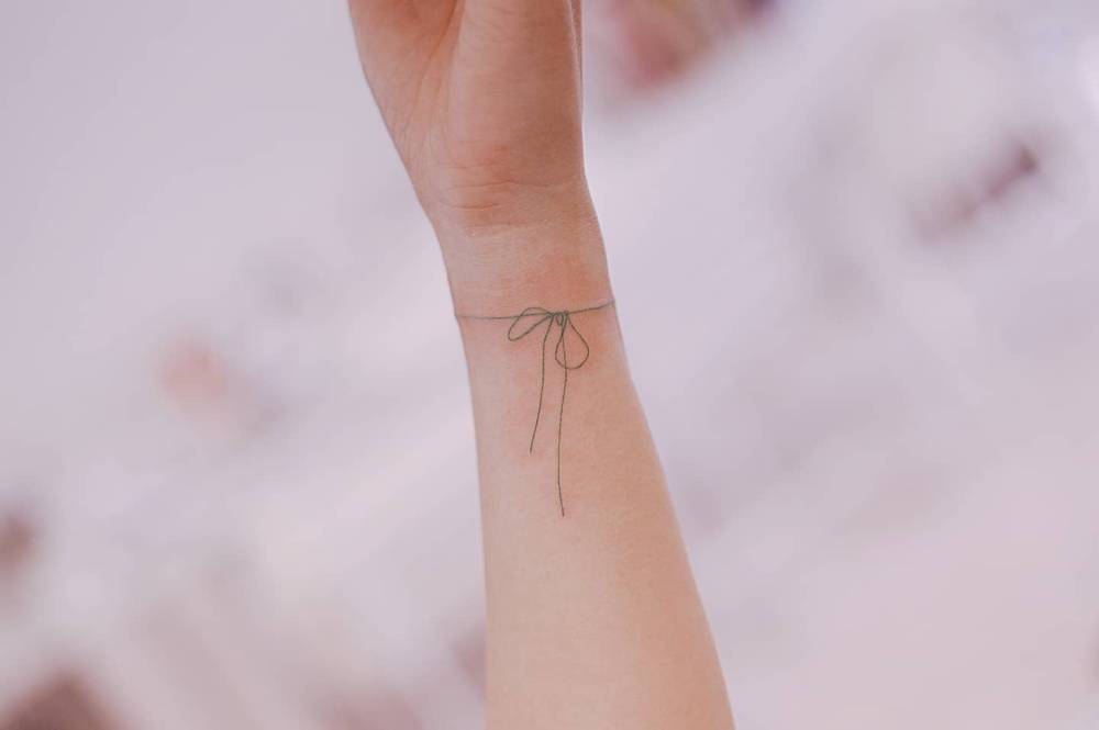 Ribbon wristband tattoo in fine line style.