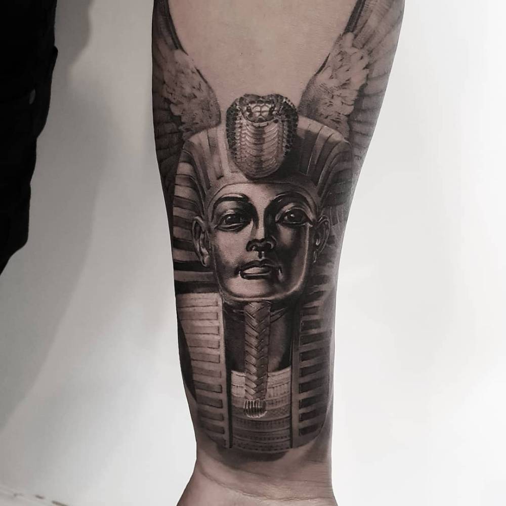Tutankhamun tattoo in black an grey style located on the wrist.