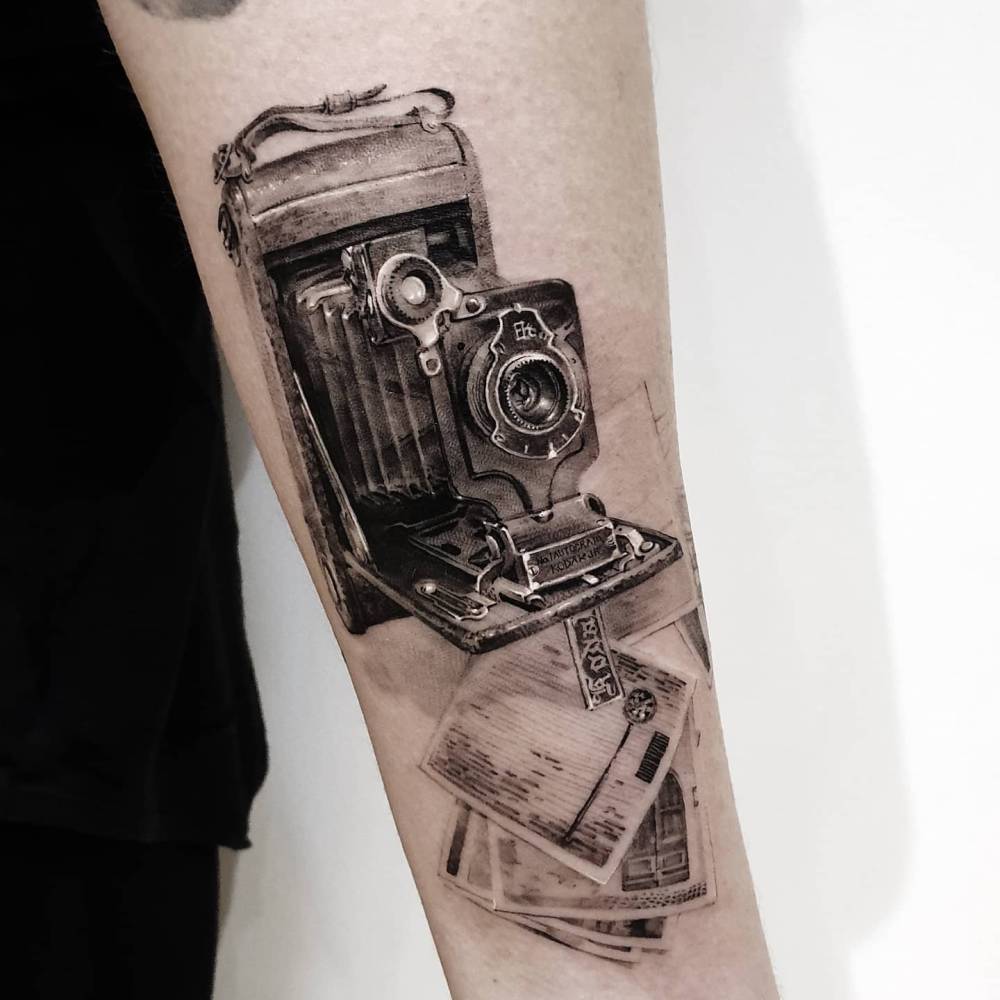 Black and grey style folding camera tattoo located on the inner forearm.