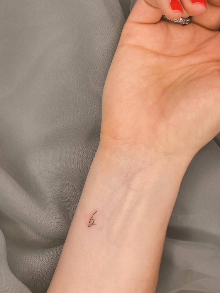 Tiny handwritten letter "B" tattooed on the wrist.