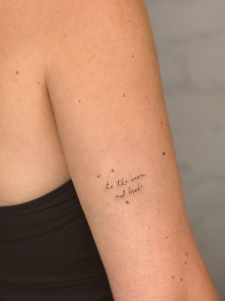 Handwritten font "to the moon and back" lettering tattoo located on the tricep.