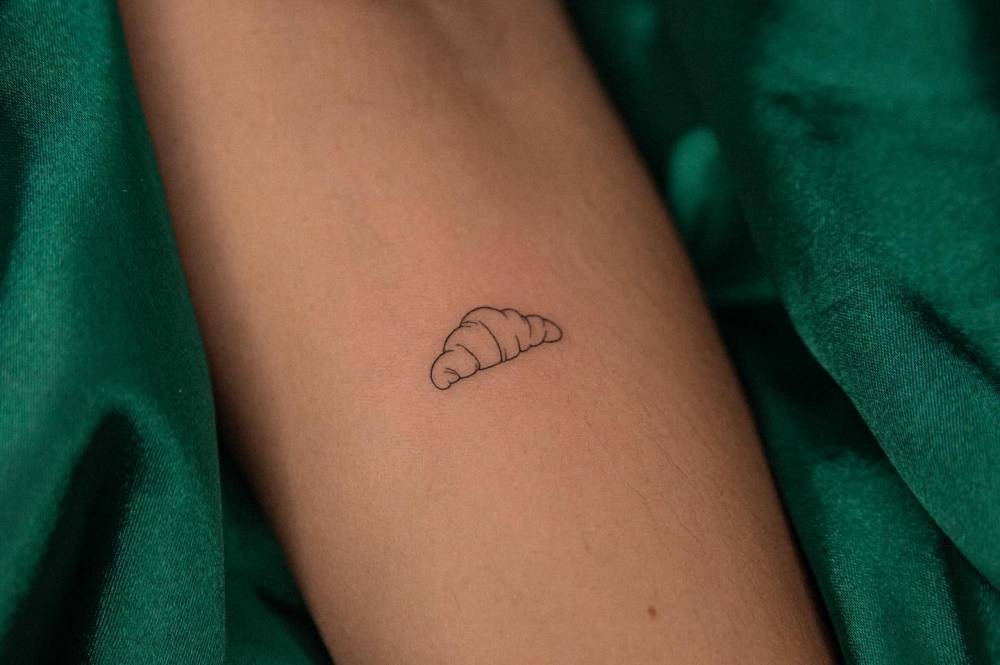 Fine line style croissant tattoo placed on the inner forearm.