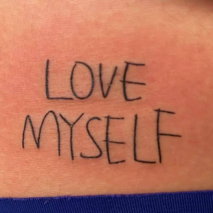 "Love myself" lettering tattoo on the lower back.