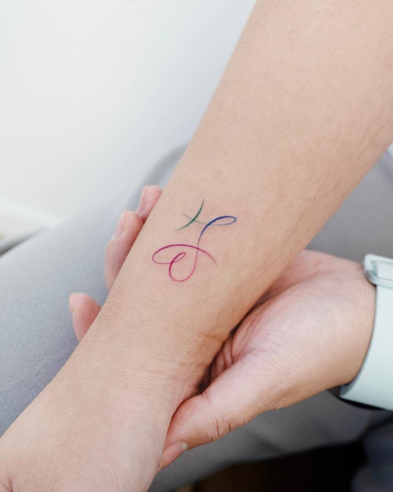 Watercolor style heart and Pisces zodiac symbol tattooed on the wrist.