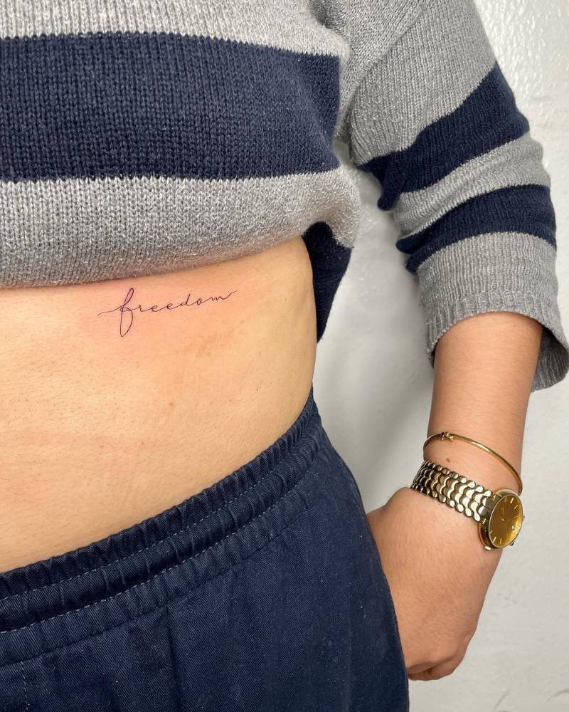Tattoo of the word "freedom" handwritten on the rib.