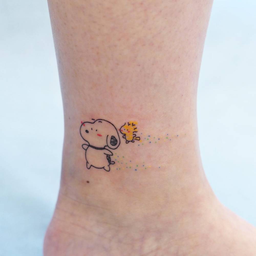 Snoopy and Woodstock in cartoon style tattooed on the ankle.