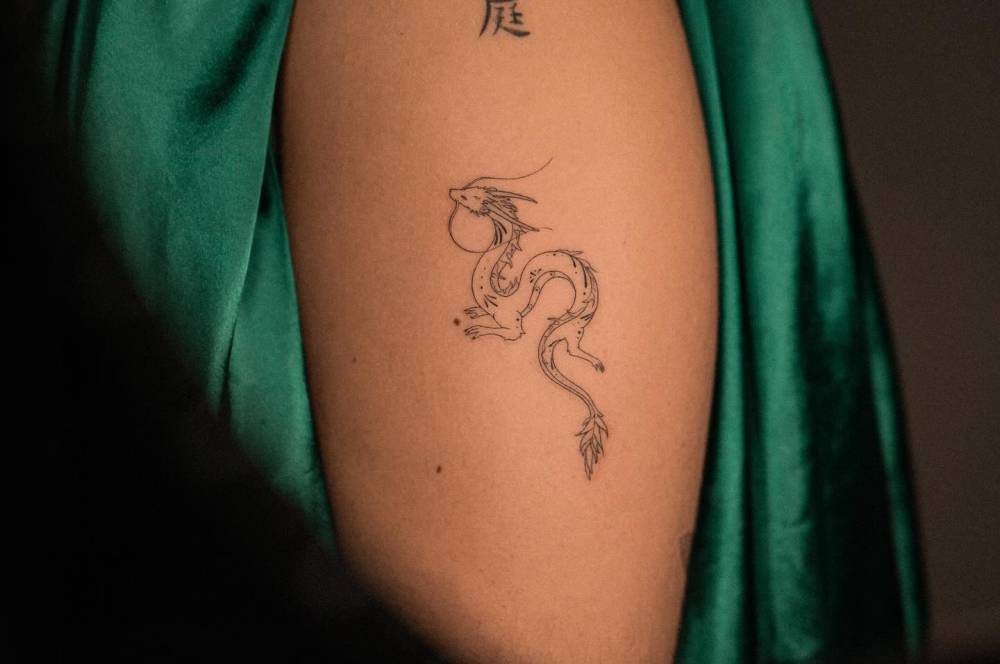 Fine line style Haku tattoo located on the upper arm.