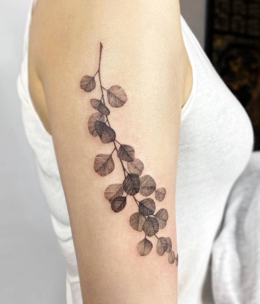 Watercolor style eucalyptus tattoo located on the upper arm.