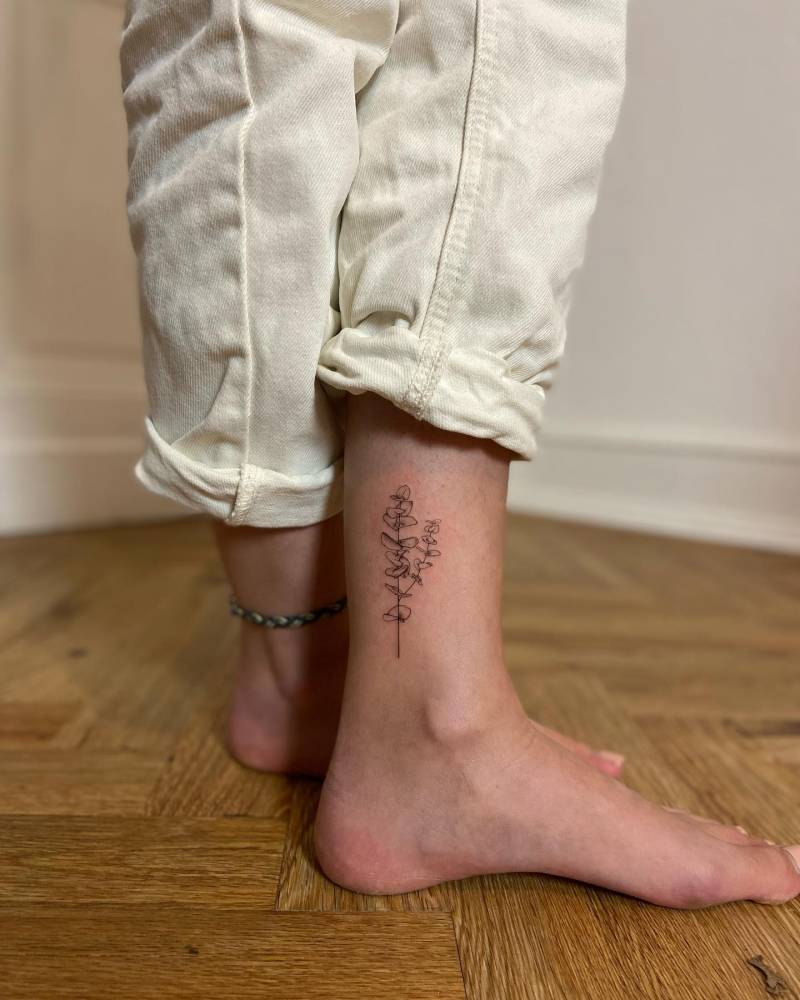 Delicate eucalyptus tattoo in fine line, placed on the ankle.