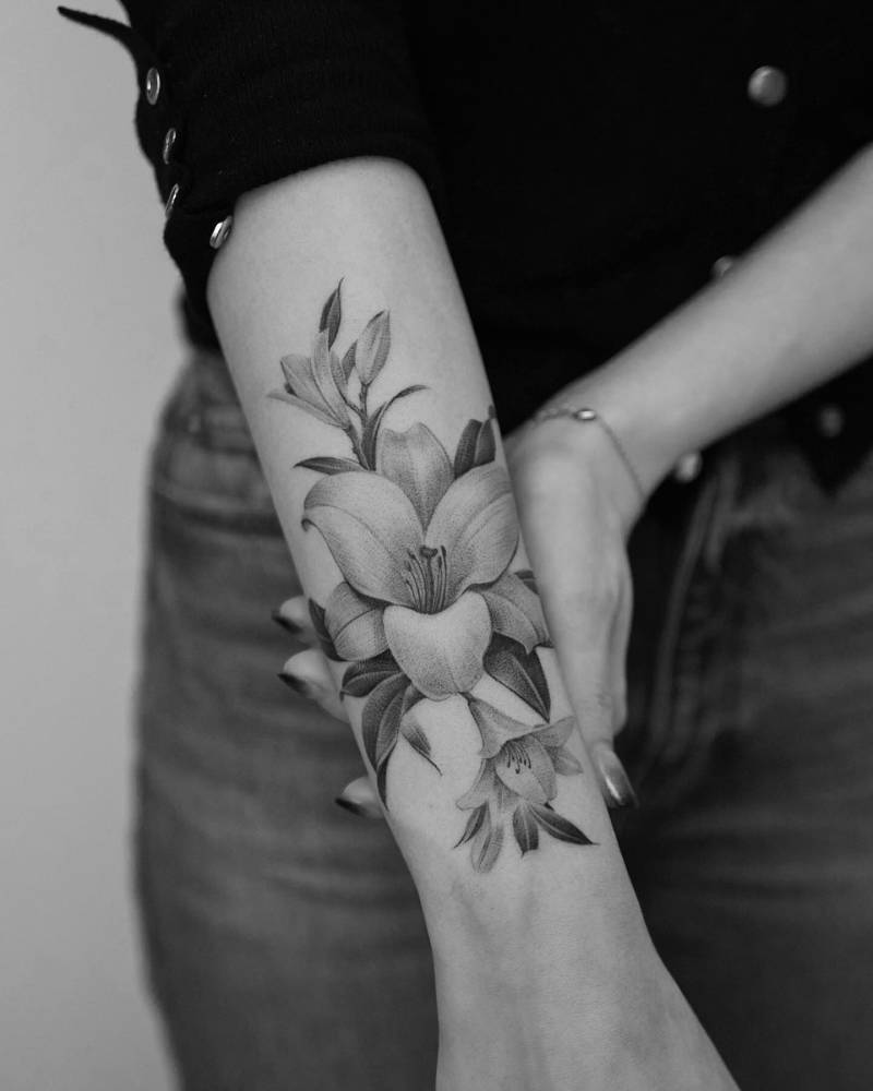 Black and grey lily flower tattoo located on the forearm.