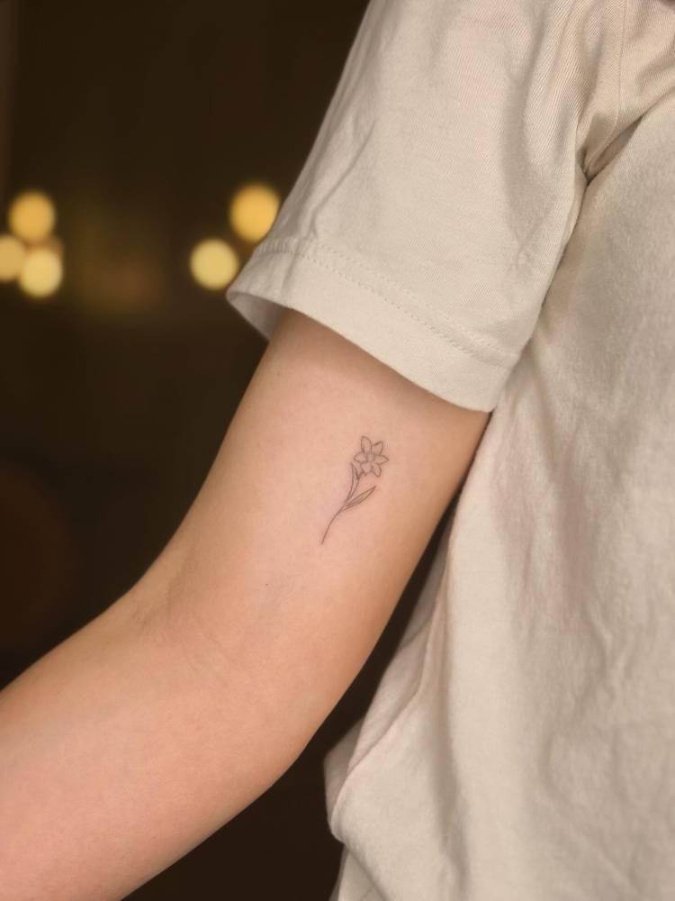 Little flower tattoo located on the inner arm, fine line style.