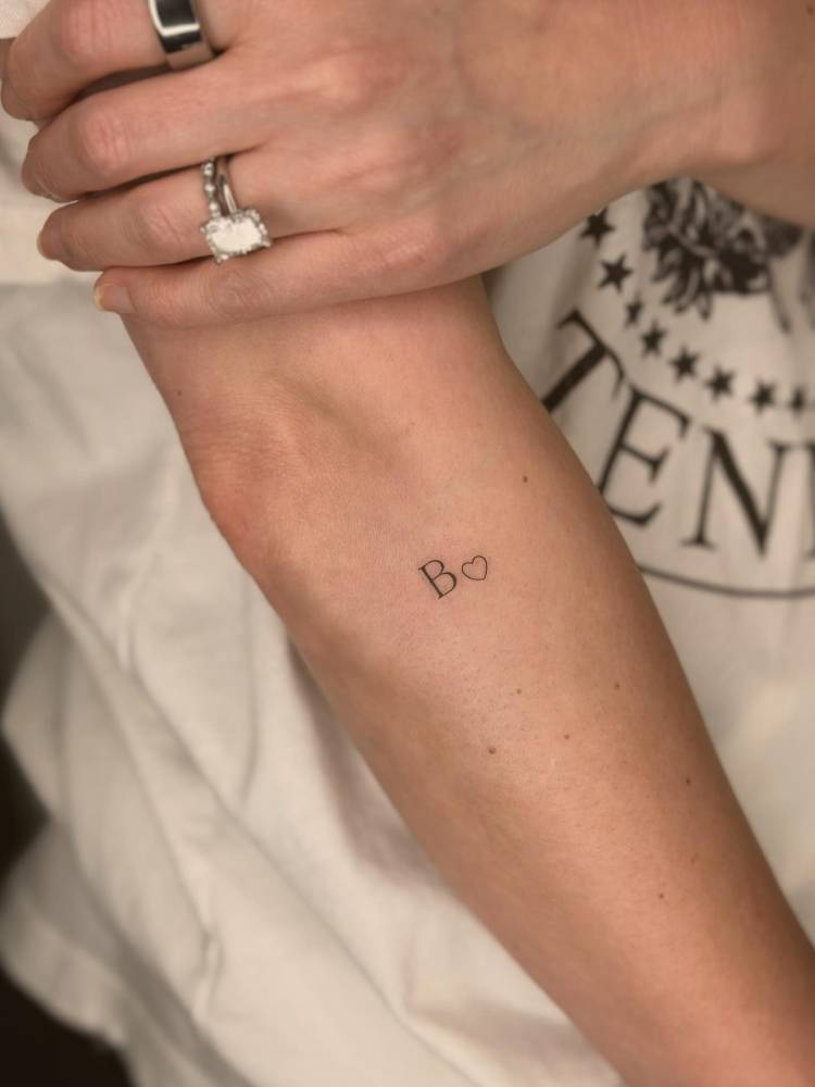 Serif font letter "B" and tiny heart tattooed on the forearm.