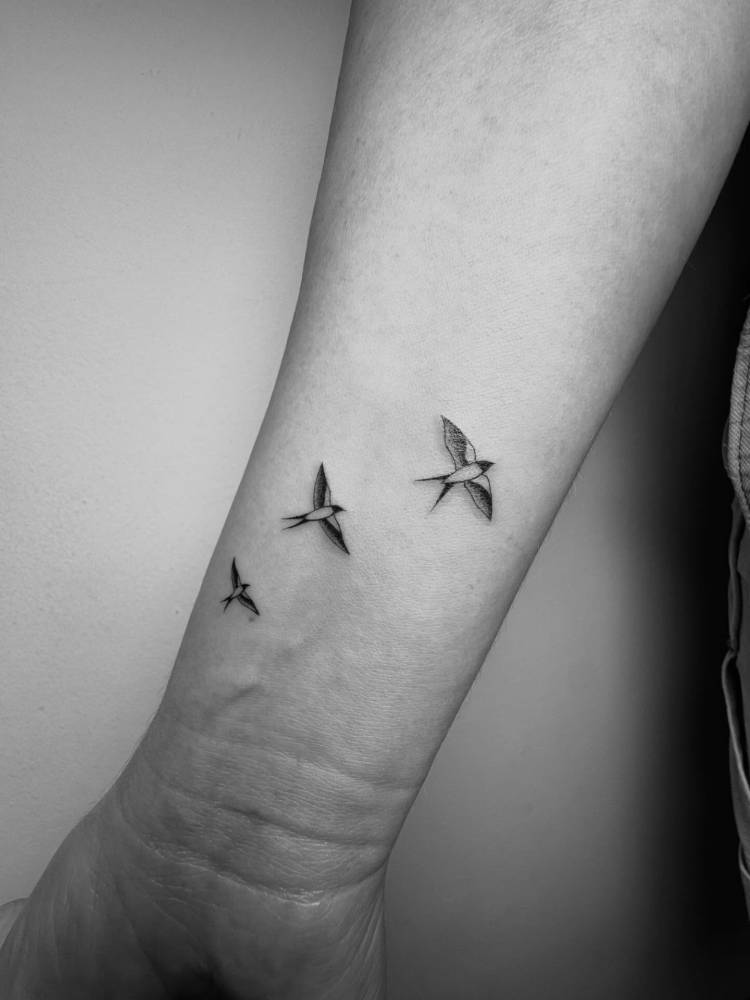 Flying swallows tattoo in illustrative style done on the wrist.