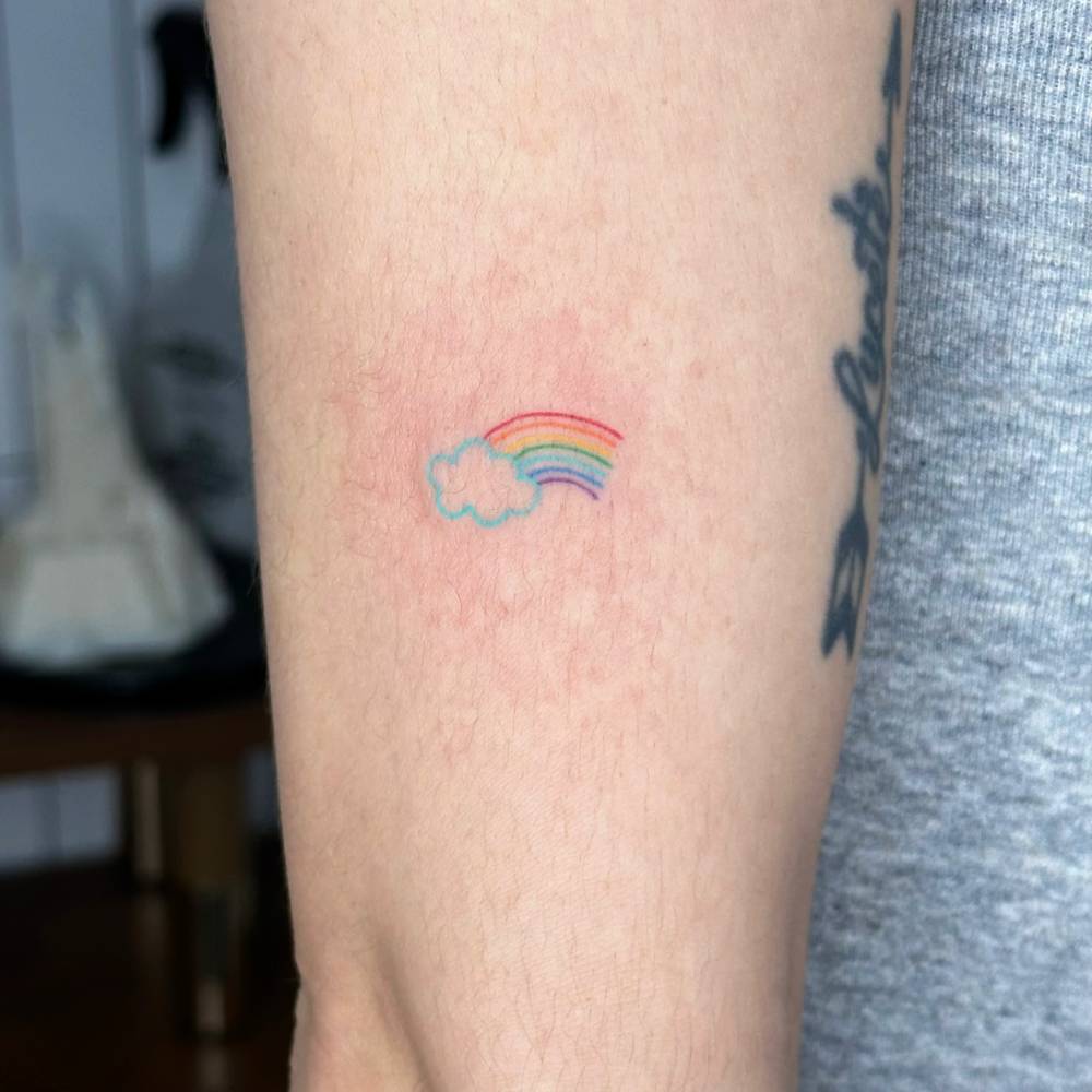 Cloud and rainbow tattoo in minimalistic style done on the upper arm.