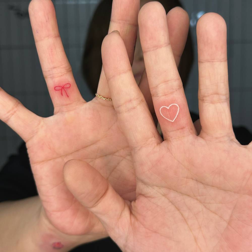 Red bow and white heart tattoos located on the fingers.