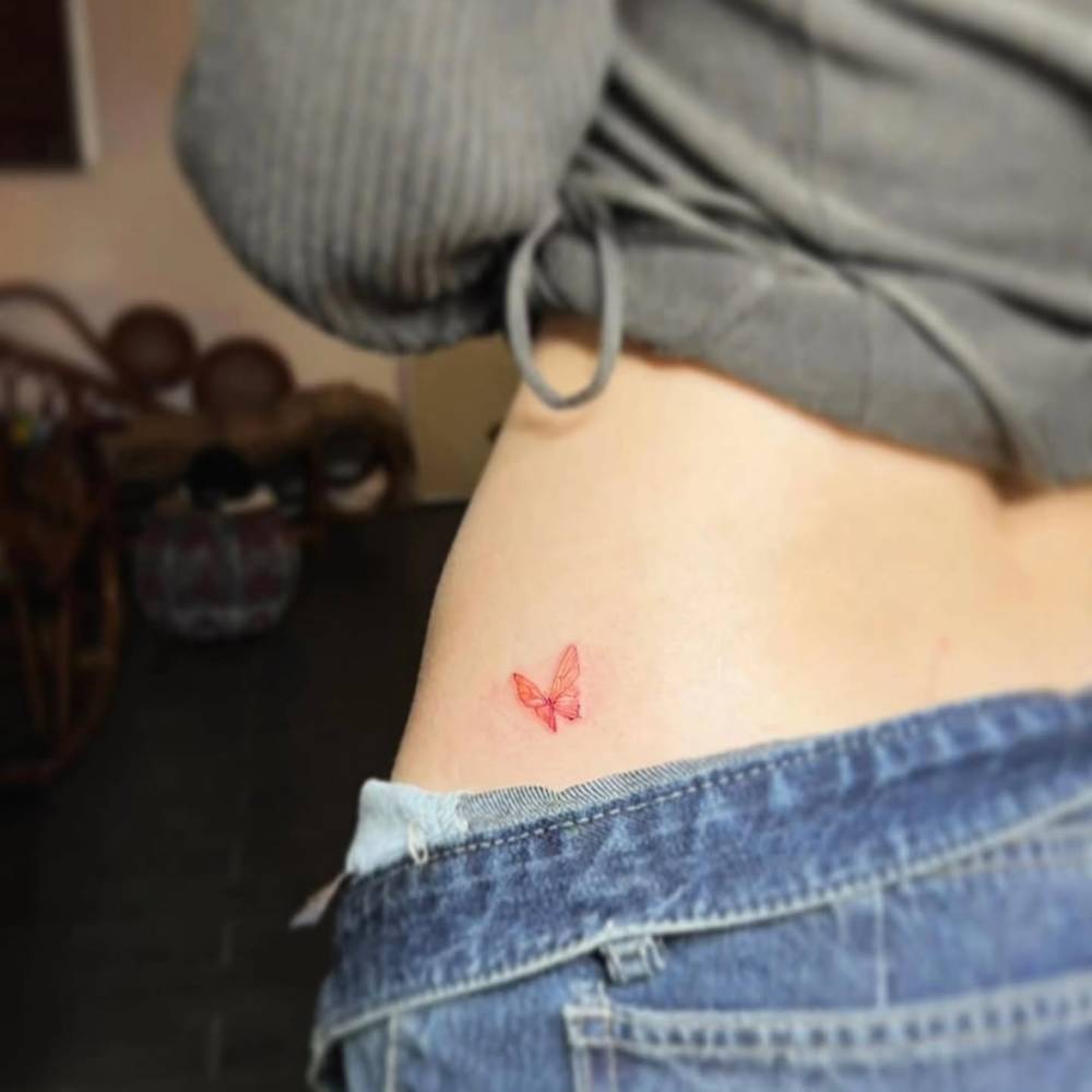 Red butterfly tattoo located on the hip, fine line style.