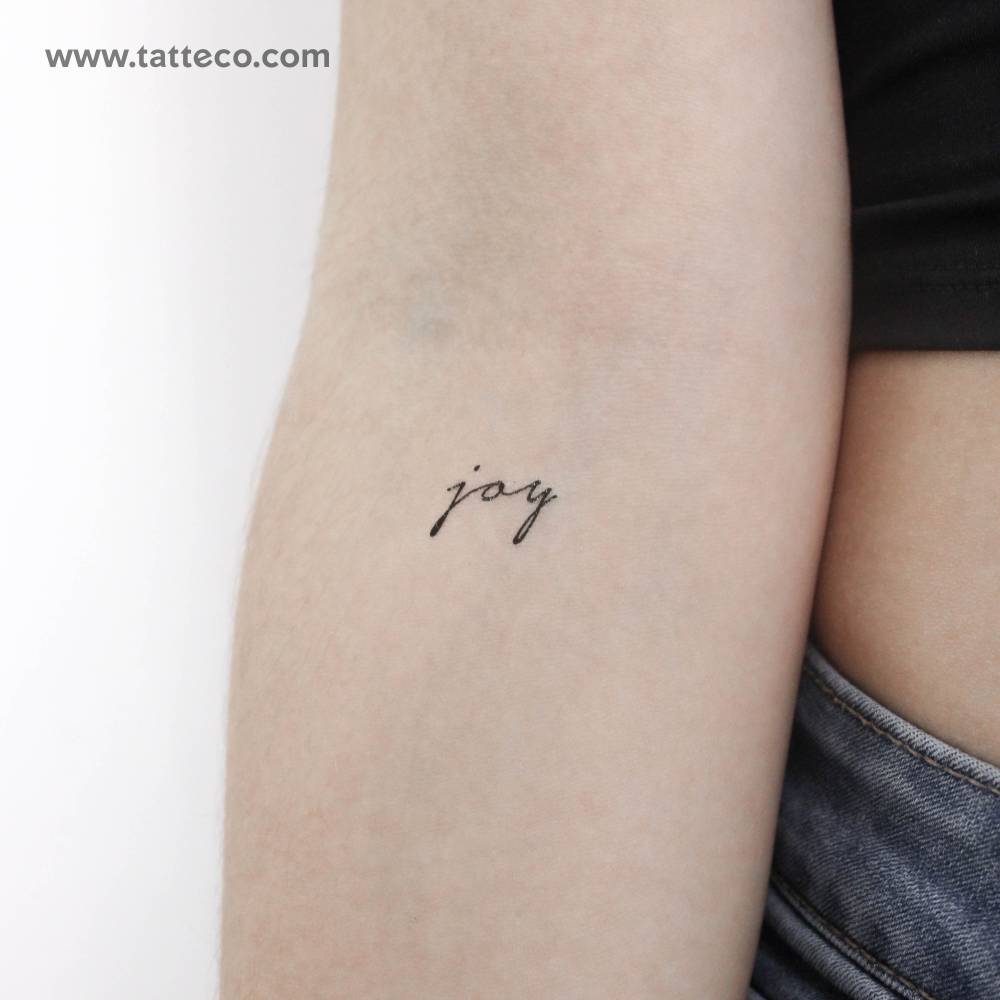 Handwritten font word "joy" temporary tattoo located on the inner forearm.