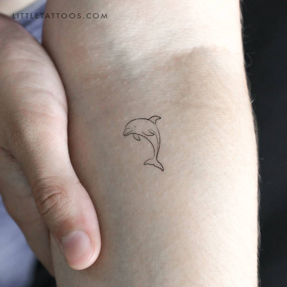 Fine line style little dolphin temporary tattoo located on the inner forearm.