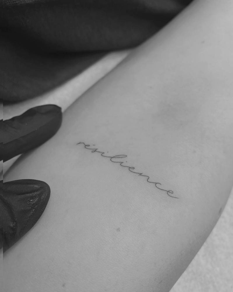 "Resilience" handwritten lettering tattoo done on the inner forearm.