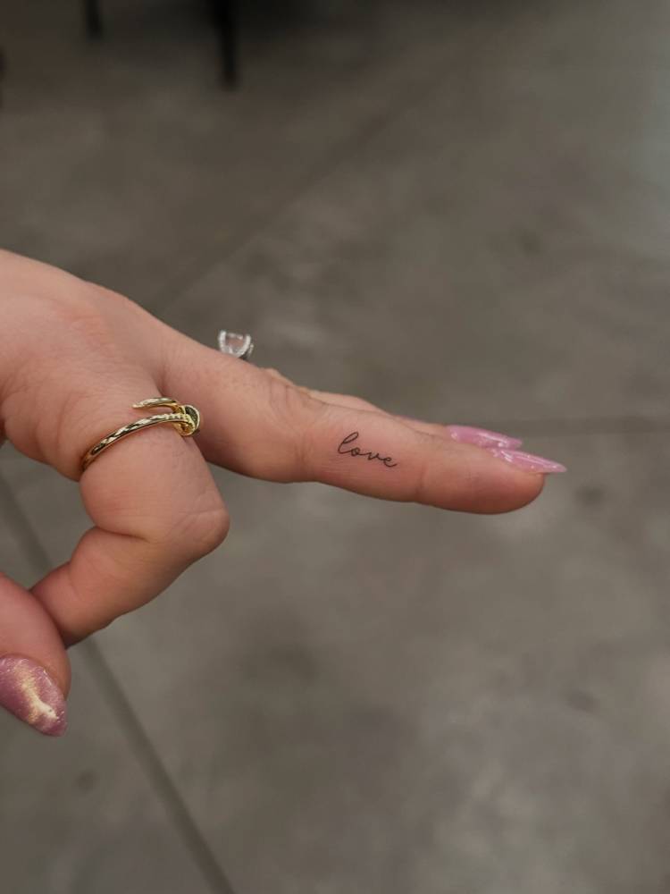 Handwritten lettering tattoo of the word "love" placed on the finger.
