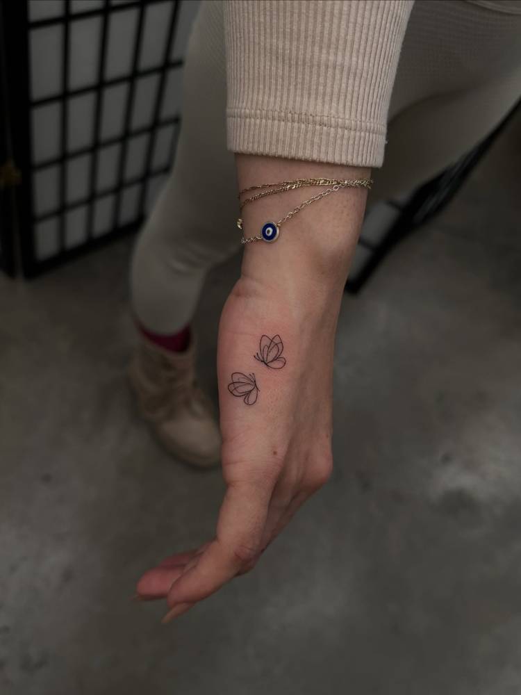 Tiny butterfly couple tattoo placed on the hand, fine line style.
