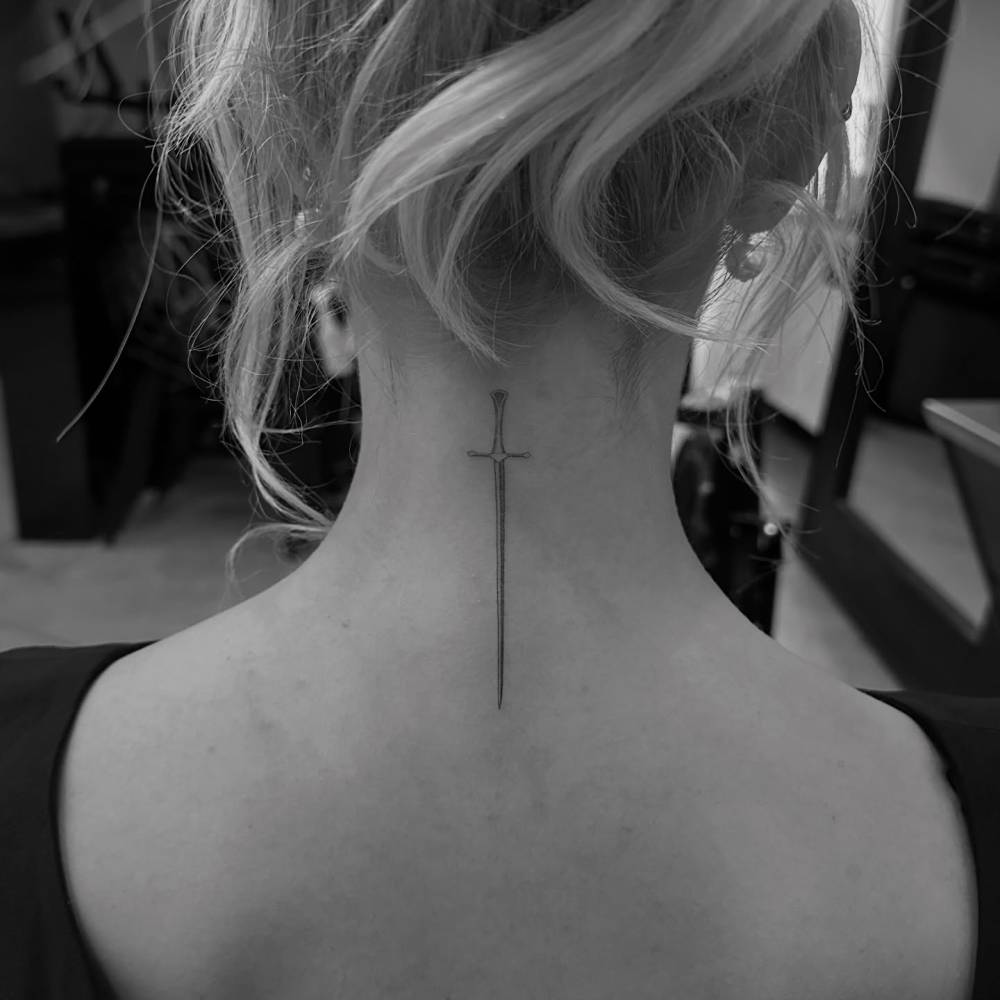 Little sword tattoo in fine line style placed on the back of the neck.