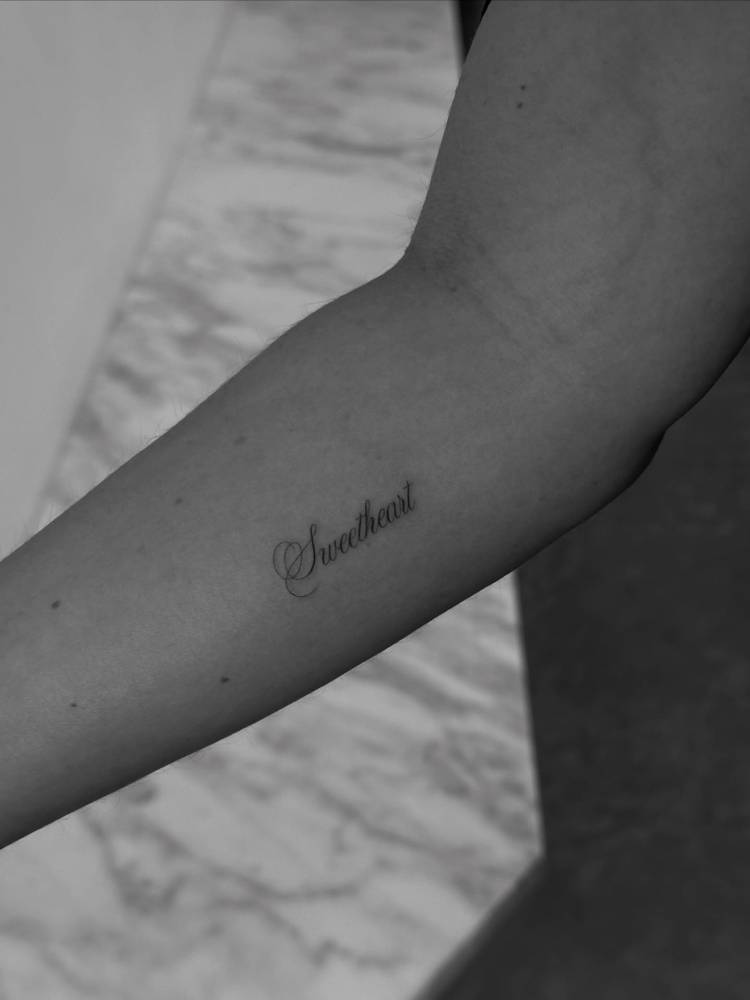 Word "sweetheart" in scrip font tattooed on the inner forearm.
