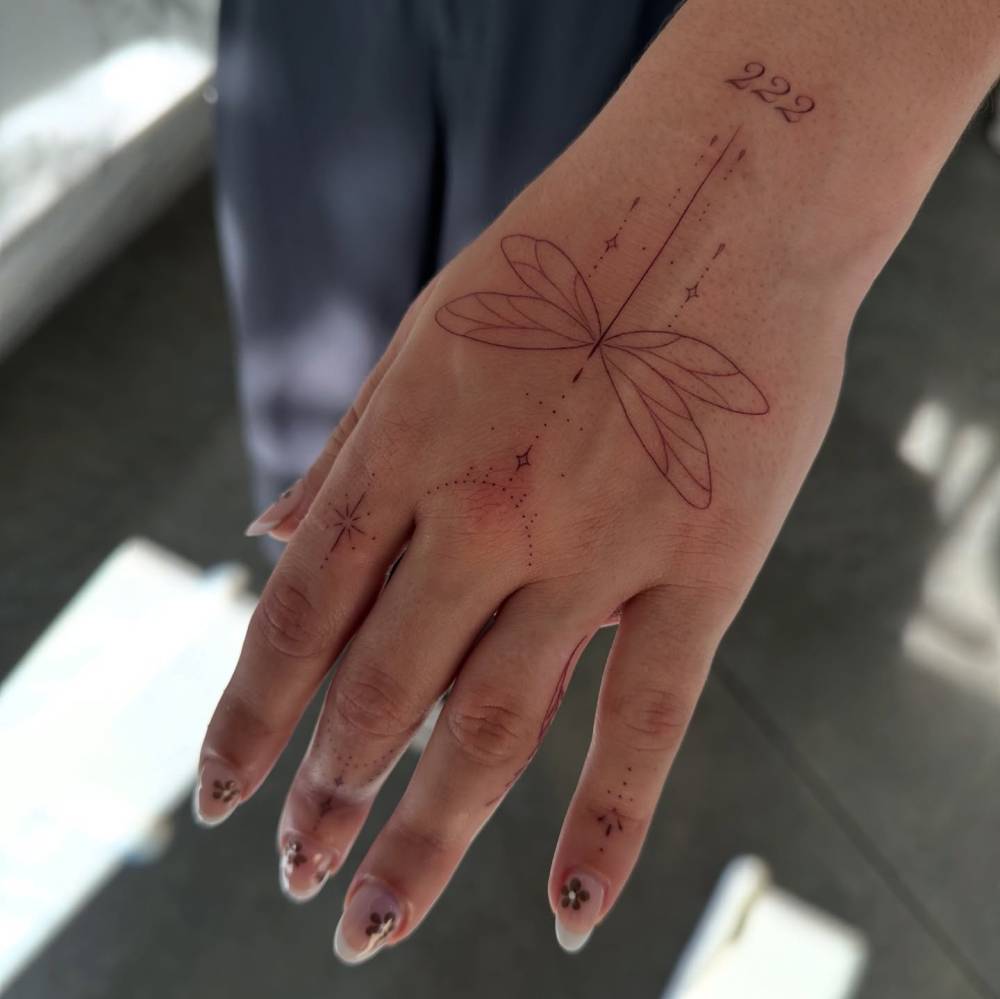 Ornamental dragonfly tattoo located on the hand, done in fine line style.