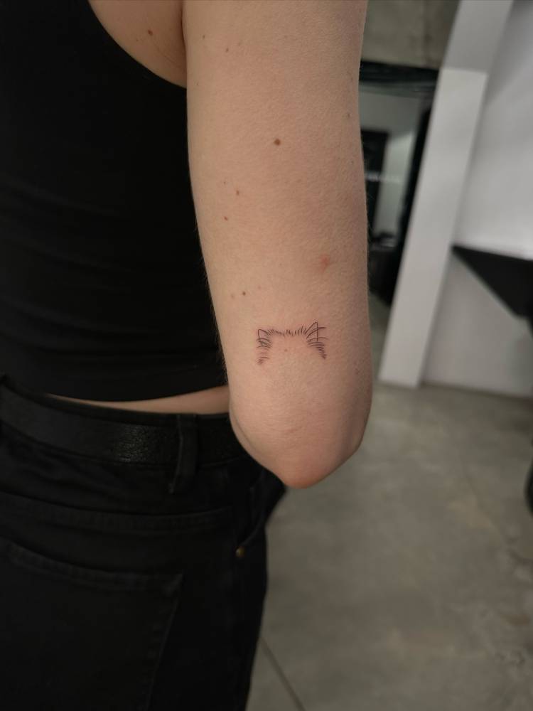 Little dog ears tattoo in fine line style placed on the tricep.