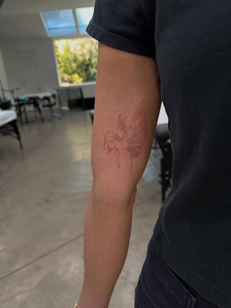 Angel in fine line style tattoo located on the inner arm.