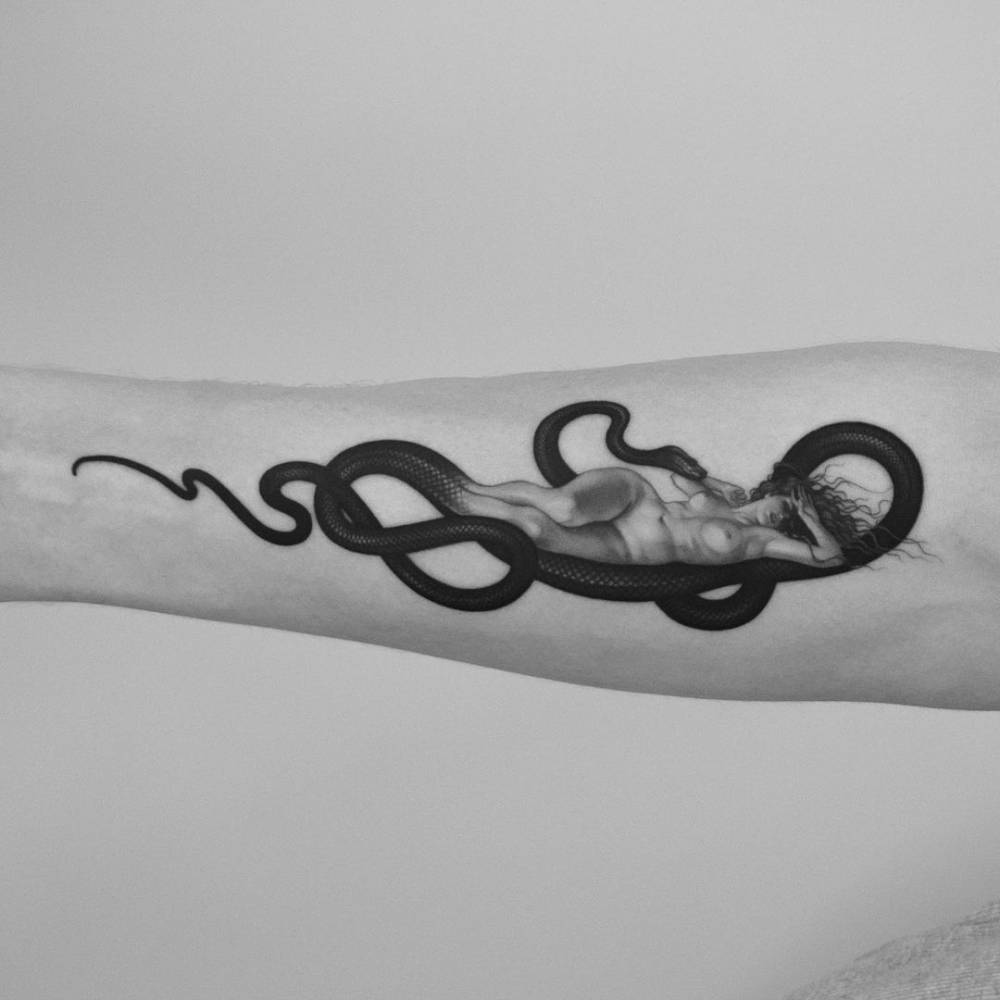 Micro-realistic snake and woman tattoo on the inner forearm.