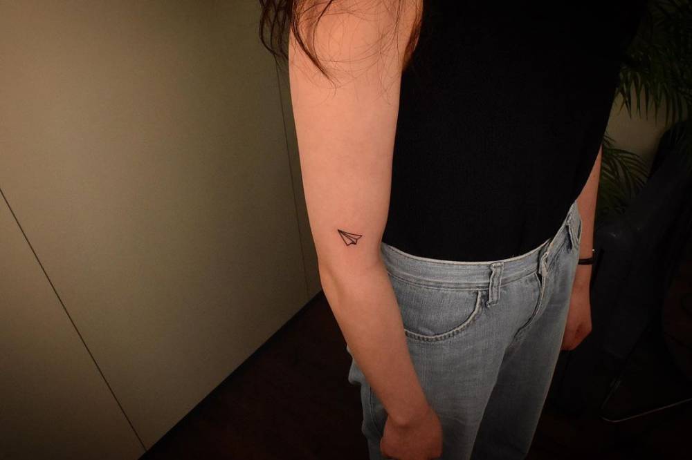 Minimalistic style paper plane tattooed on the upper arm.