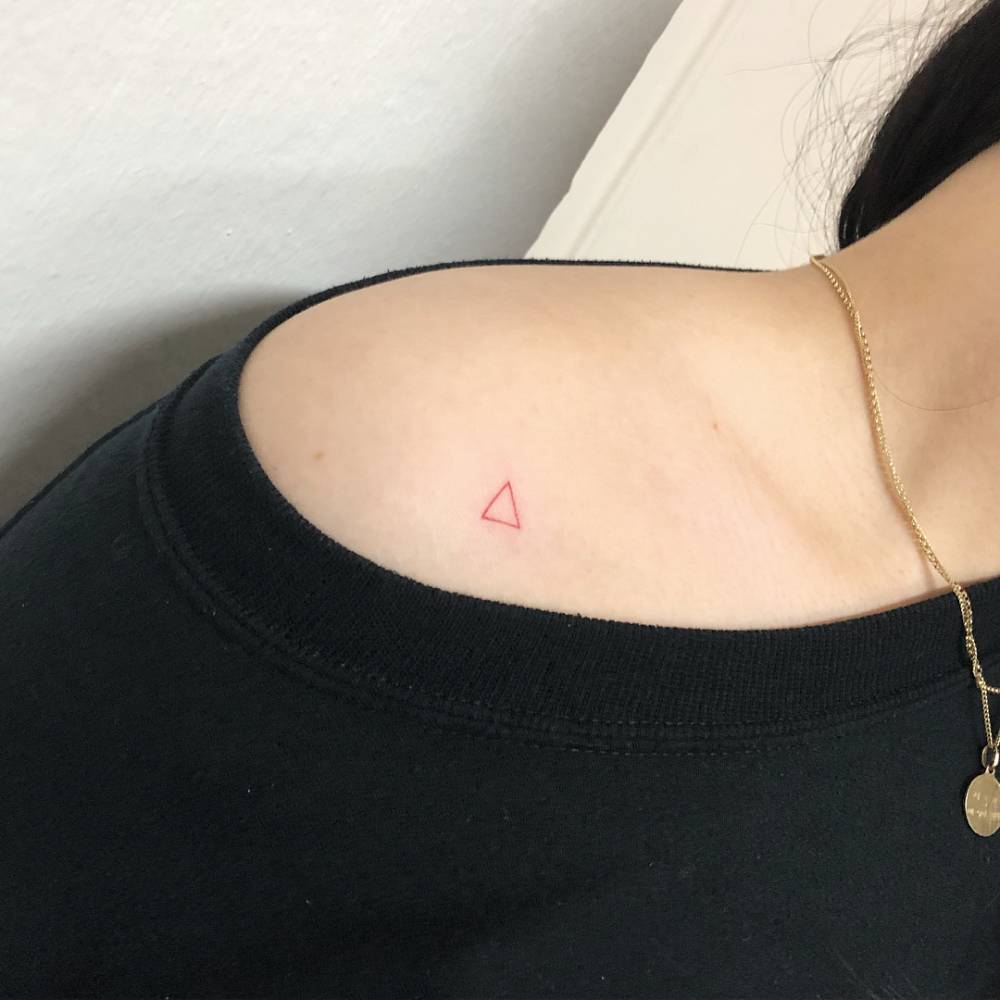 Minimalistic style red triangle tattoo located on the shoulder.